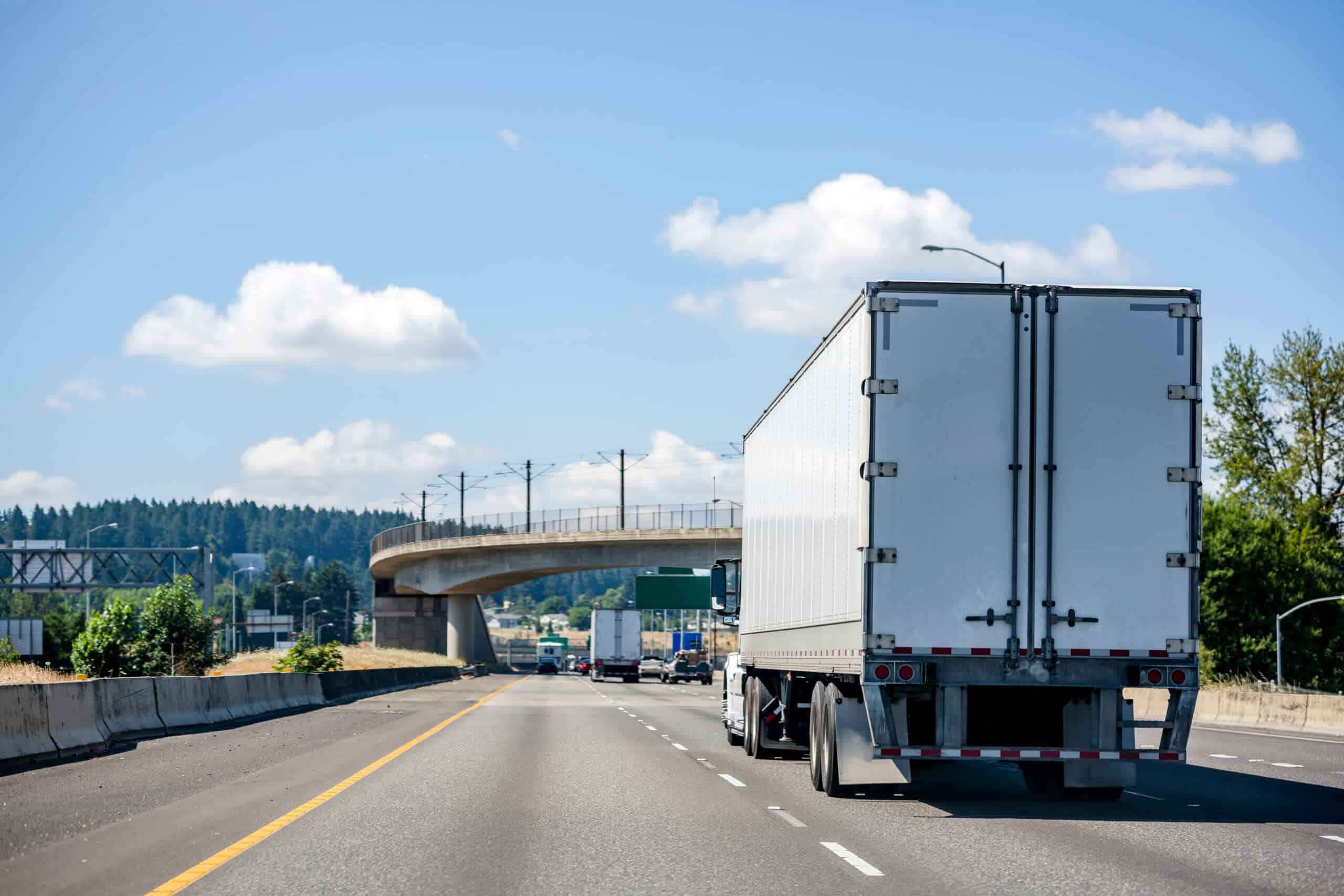 Commercial truck driving on highway with bridge in background.