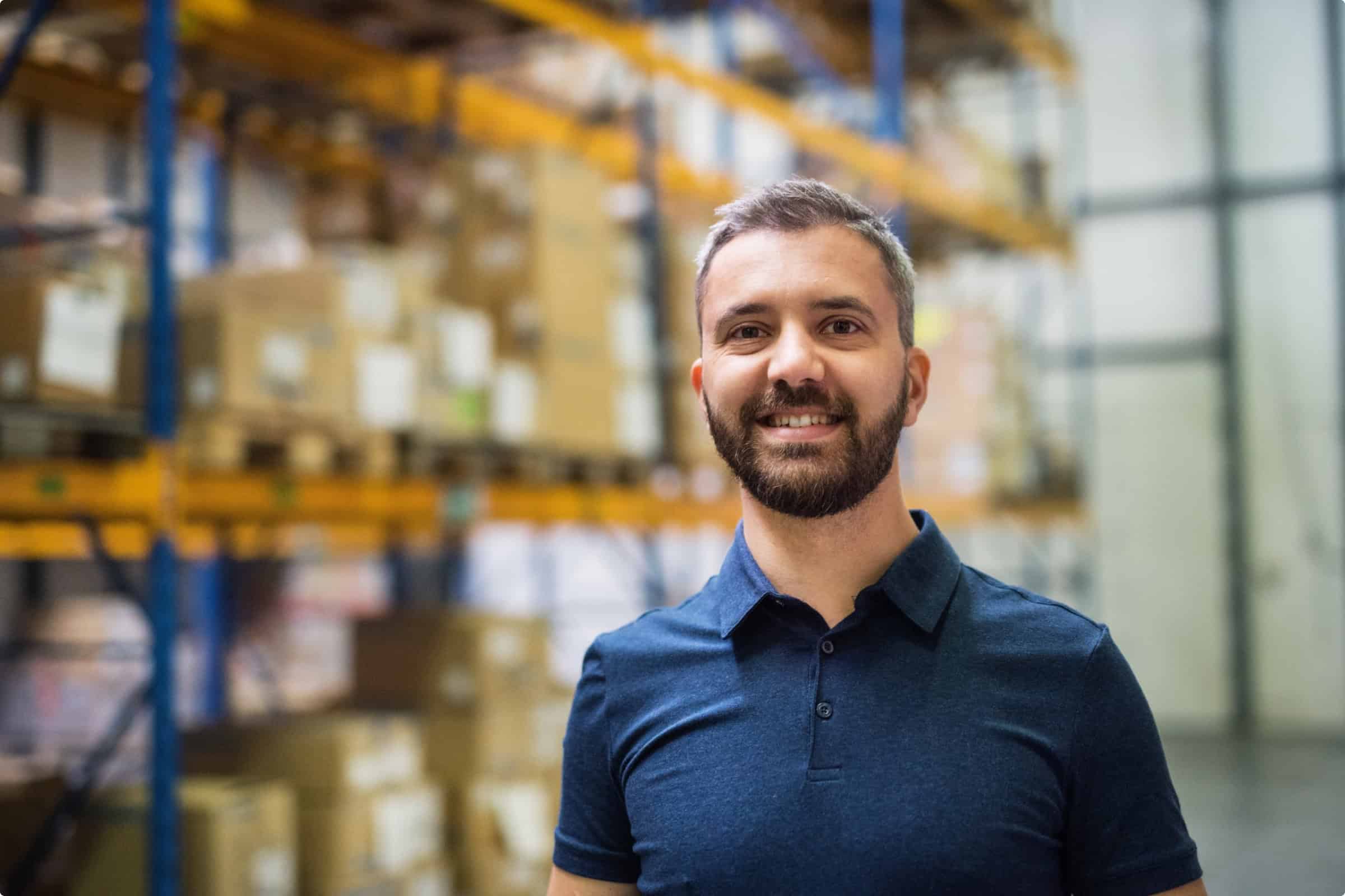 Warehouse worker smiling in a distribution center with shelves of boxes.