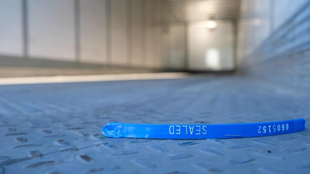 Broken blue cargo trailer security seal lying on the floor of an empty semi-trailer, symbolizing cargo theft, freight fraud, supply chain security breaches, and transportation risk.