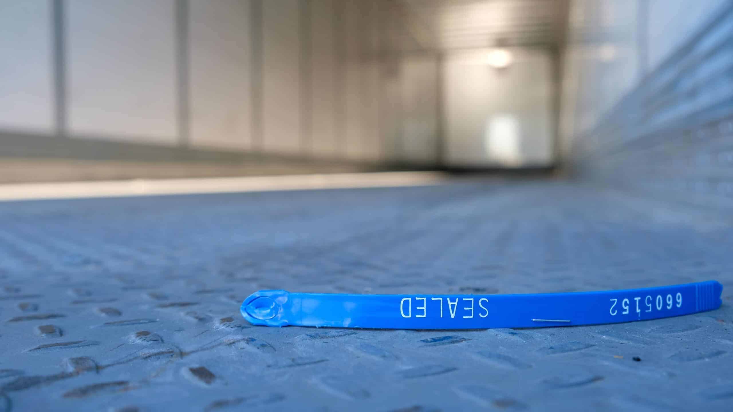 Broken blue cargo trailer security seal lying on the floor of an empty semi-trailer, symbolizing cargo theft, freight fraud, supply chain security breaches, and transportation risk.